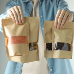 Woman with stand-up pouches of different products on light grey background