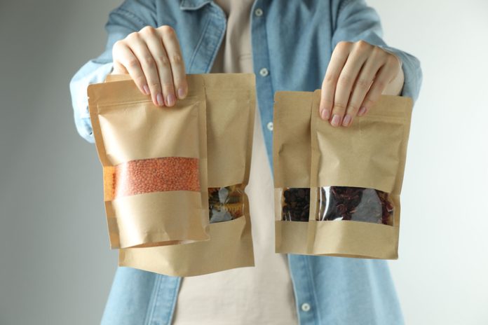 Woman with stand-up pouches of different products on light grey background, closeup Woman with stand-up pouches of different products on light grey background