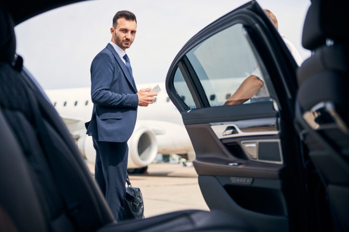 Successful businessman standing by the car looking determined Logan Airport pickup service