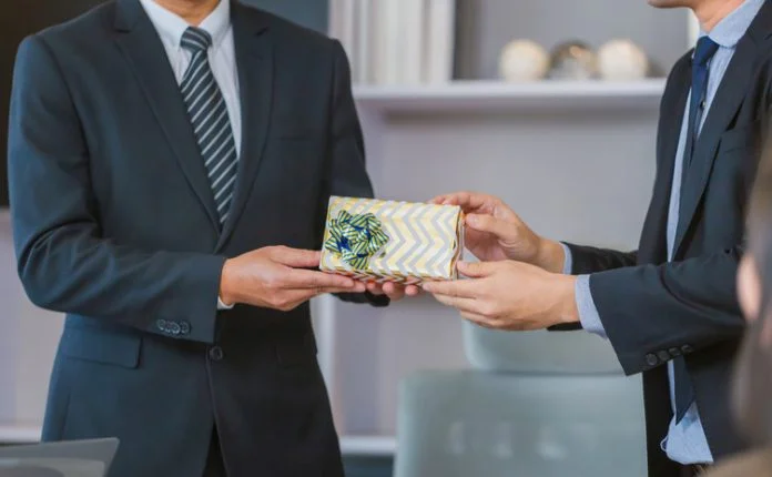 Young businessman giving his colleague present in office, Close-up view of hand man giving a gift box to a friend B2B gifting