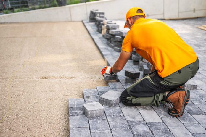 Worker Laying Cobblestones for a Patio in a Residential Backyard on a Sunny Day
