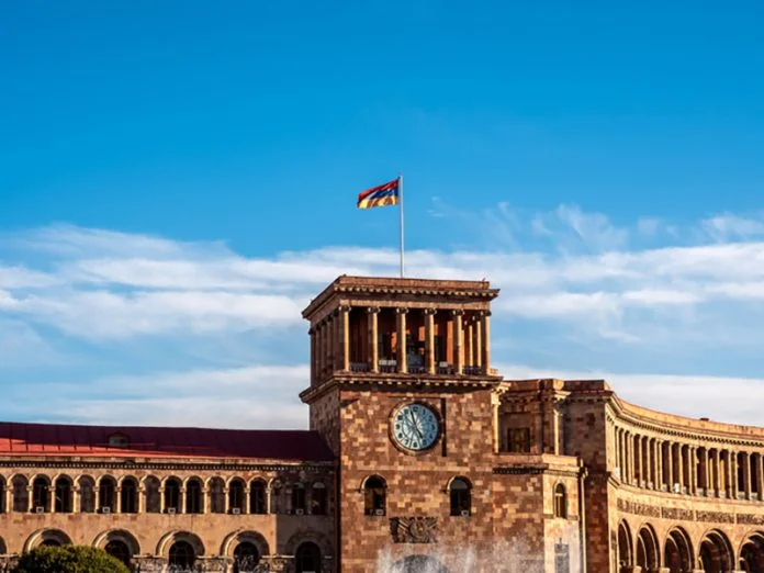 Scene of the clock bell tower with flag on top, on blue sky background on sunny day, near the government building and republic square, historical landmark in Yerevan, Armenia. Armenia's First International Startup Campus