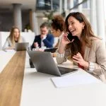 marketing channel through phone calls. Woman talking over smart phone while sitting with laptop