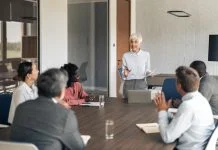 Mature businesswoman holding documents and speaking with her personal board l group of employees during a corporate meeting in a modern office boardroom