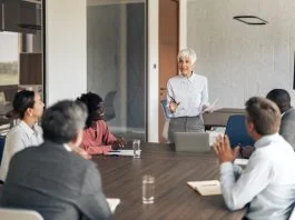 Mature businesswoman holding documents and speaking with her personal board l group of employees during a corporate meeting in a modern office boardroom