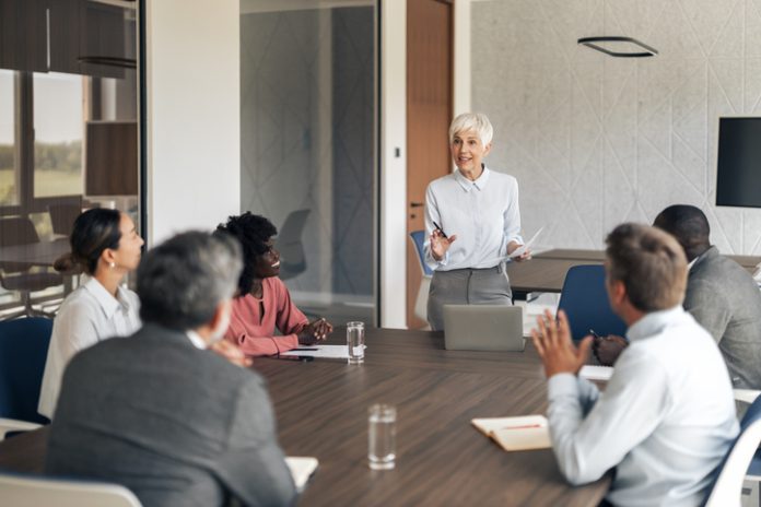 Mature businesswoman leading business meeting discussing corporate strategy Mature businesswoman holding documents and speaking with her personal board l group of employees during a corporate meeting in a modern office boardroom