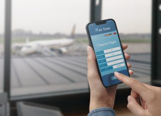 How Seasonal Travel Trends Affect Flight Costs (and When to Book Your Shoulder-Season Trip) User holding a smartphone and booking cheap flights online, seasonal travel trends, airport in the background.