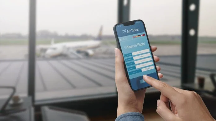 User holding a smartphone and booking cheap flights online, seasonal travel trends, airport in the background.