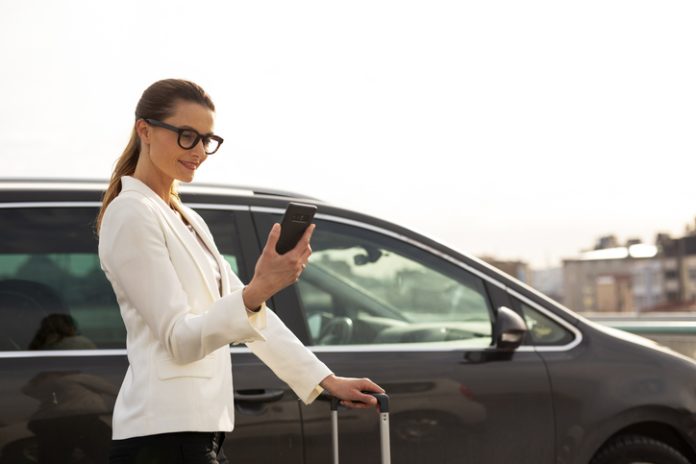 Businesswoman with luggage walking to the car on parking. corporate travel planning