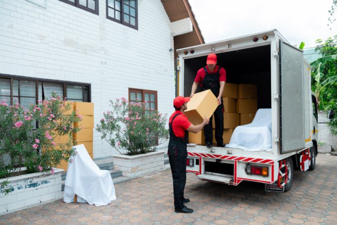 Indian and Caucasian partnership mover workers in red uniform uploading furniture and boxes to new house, shipping company small business owner using delivery truck sending packages to customers relocation costs