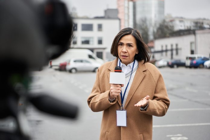 Journalist in a coat reports live at a city location amidst cold, gray weather news reporter Kelli Stavast