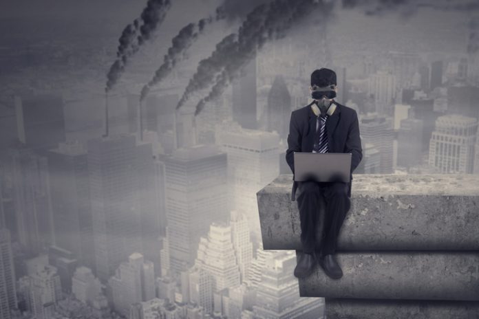 Worker with laptop and air pollution Male worker working on the rooftop while using laptop computer and wear a gas mask with air pollution in the city, Companies operating despite the negative impact on society concept.