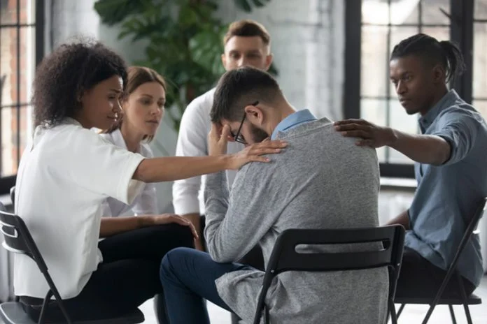 Diverse people supporting unhappy man at therapy session, touching shoulders. What Employers Can Do to Support Staff Struggling with Addiction