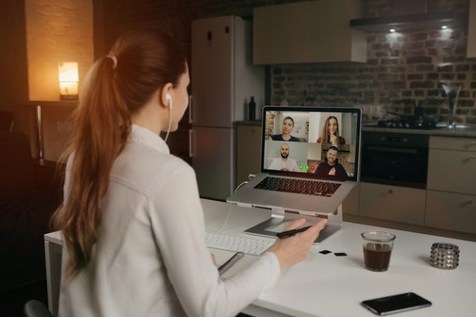 Back view of a woman talking to her colleagues in a video conference on laptop. Cross-Device Messaging for Distributed Teams