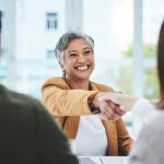 The Dog-Eat-Dog World of ‘Work Perks’ Handshake, job interview or business people with a happy mature woman for partnership in office. smile or business people shaking hands for success, work perks, promotion or negotiation in meeting