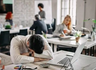 Presenteeism - Overworked businessman taking a break from work and napping on his desk.