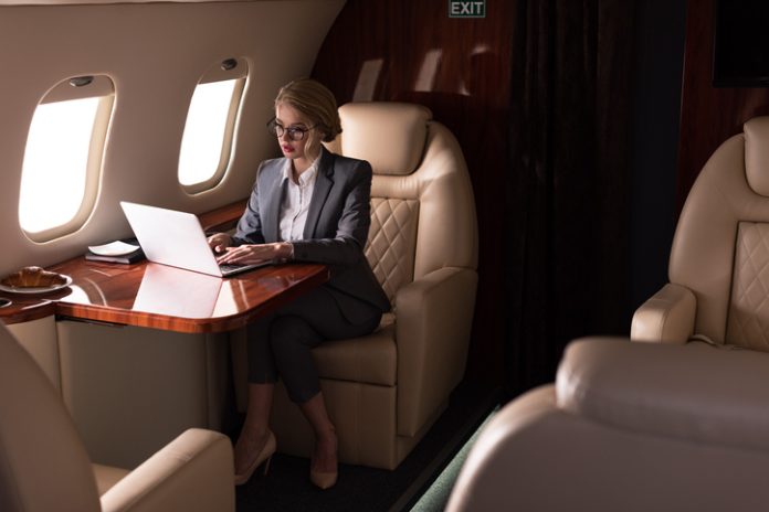confident businesswoman working on laptop in plane during business trip C-suite executives private aviation