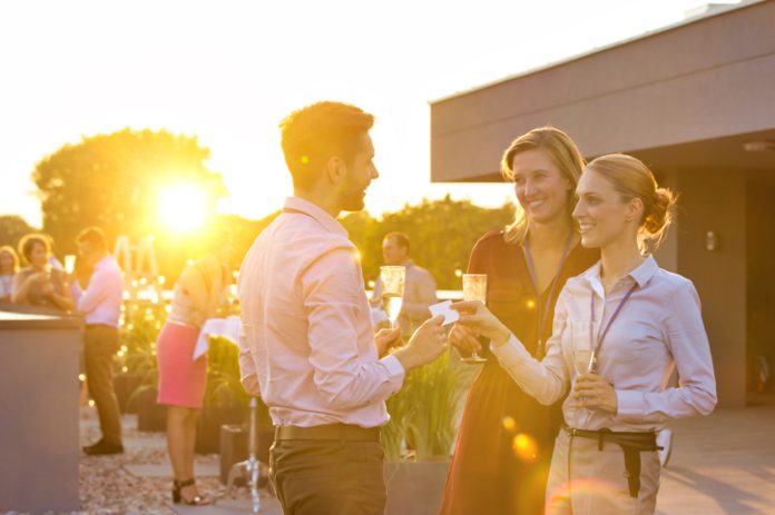 Businesswoman giving calling card to businessman in rooftop success party with yellow lens flare Outdoor Business Event