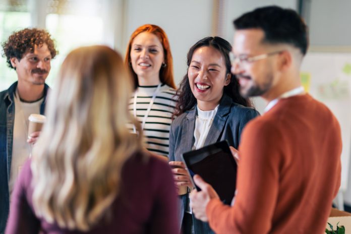 Happy diverse colleagues have fun at lunch break in office, smiling multiracial employees laugh and talk drinking coffee