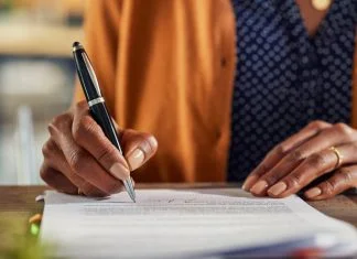 Close up of african american business woman hand writing on report while working in office. Successful black businesswoman signing documents at home using a pen.