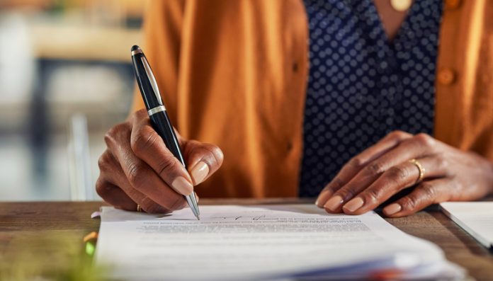 Detail of black woman hands writing on paperwork Close up of african american business woman hand writing on report while working in office. Successful black businesswoman signing documents at home using a pen.