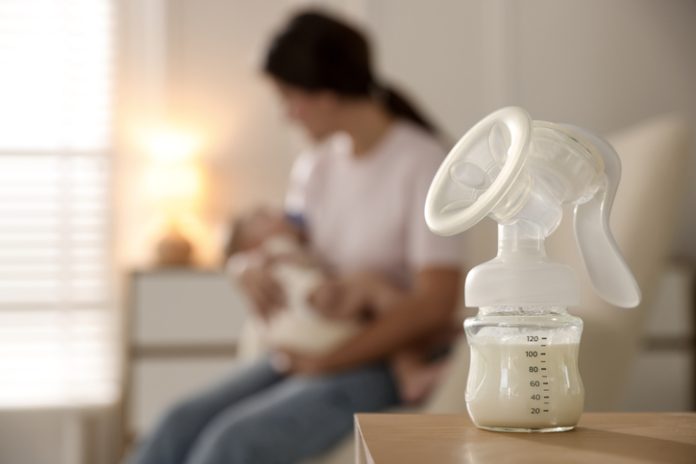 Mother holding her little baby indoors, focus on breast pump with milk Breast Pump