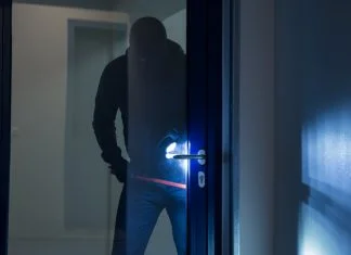 Full length of burglary using crowbar to open glass door at night