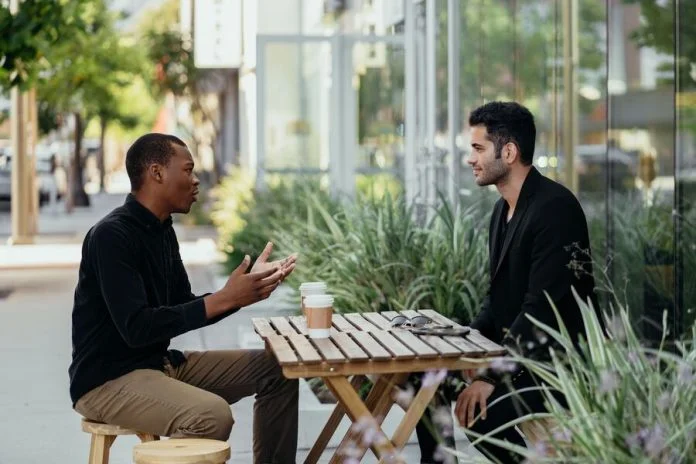 Two men talking over coffee at a small table outside a cafe. Value in business concept