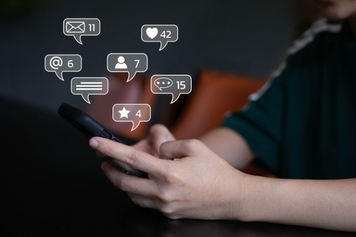 Close-up of a person using smartphone with social media notification icons. Concept of digital communication, online interaction, social networking, and mobile technology in daily life. Social Media Presence