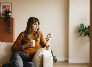 Woman relaxing on a sofa, drinking from a mug and using her phone during Free Time