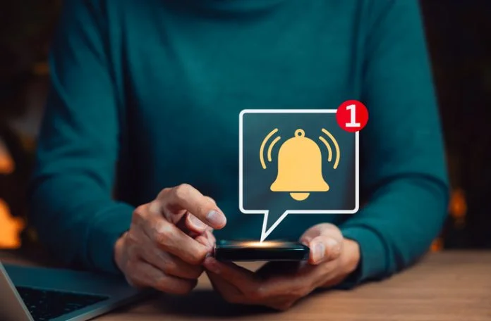 Mobile notification alert concept. Man hands holding smartphone with glowing bell icon and message indicator, symbolizing real time alerts, reminders, digital communication, and user engagement. Mobile notification alert concept.