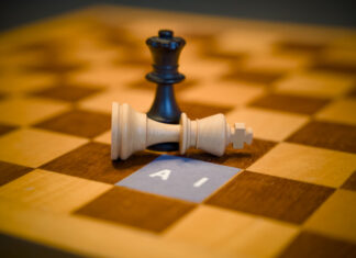 Black queen chess piece standing over a fallen white king next to a paper label reading AI, artificial intelligence dominance concept.