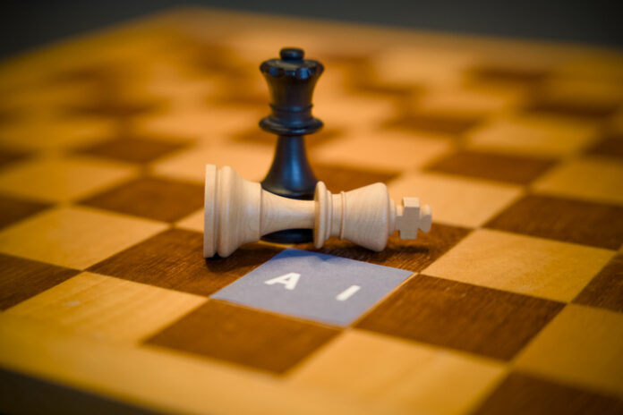 Black queen chess piece standing over a fallen white king next to a paper label reading AI, artificial intelligence dominance concept.